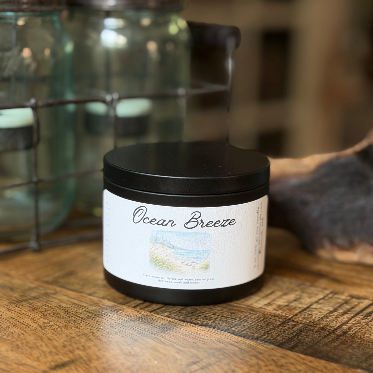Candle tin labeled 'Ocean Breeze' on a wooden surface with jars in the background