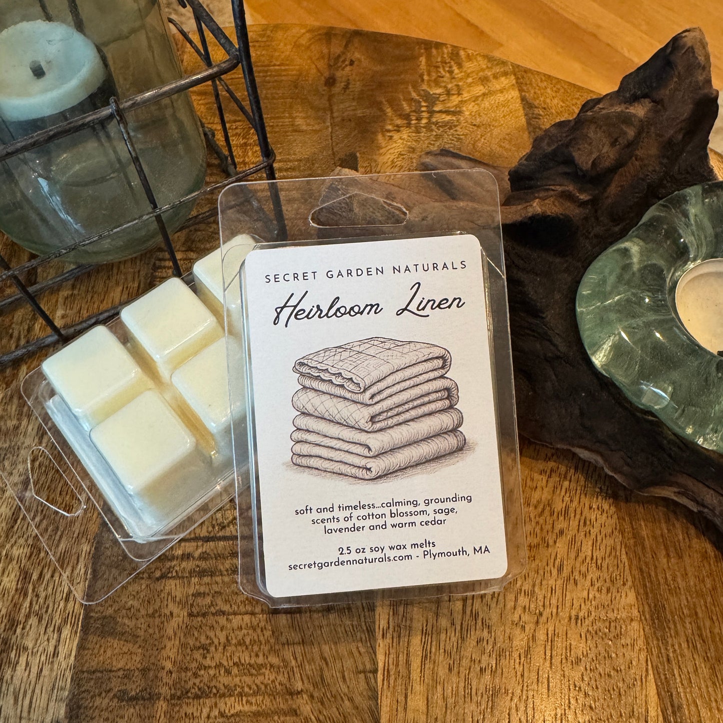 Packaged Heirloom Linen wax melts on a wooden surface with a candle in the background