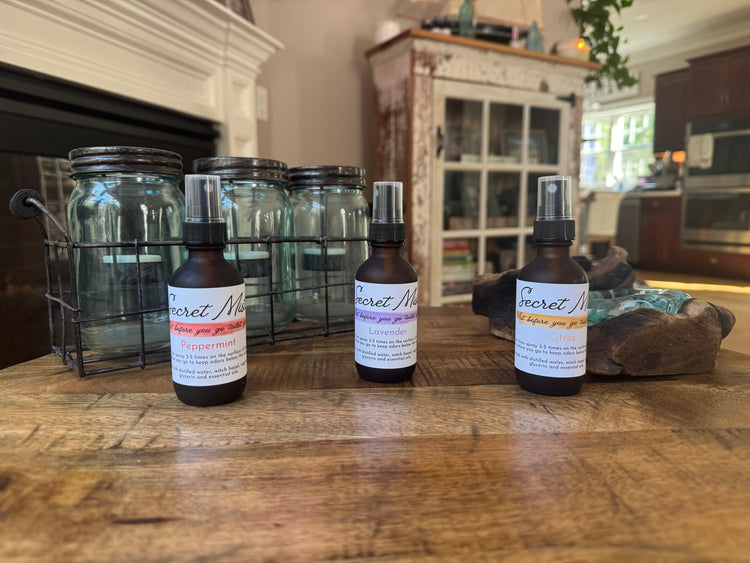 3 bottles of Secret Mist toilet spray on a wooden surface.
