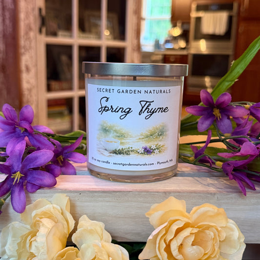 Spring Thyme candle on a wooden surface with purple and yellow flowers.