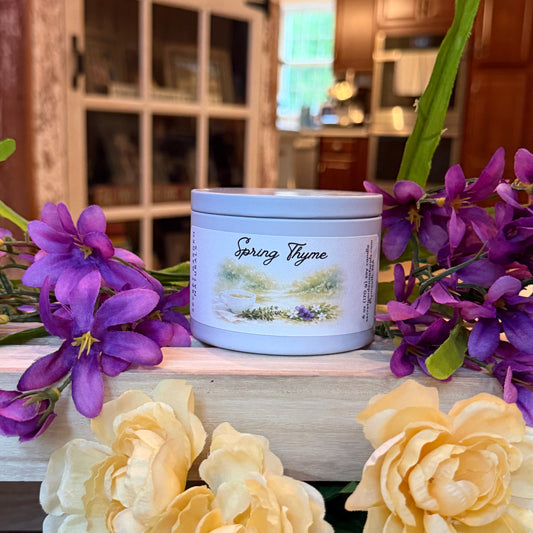 Spring Thyme candle in a white tin on a wooden surface with yellow and purple flowers