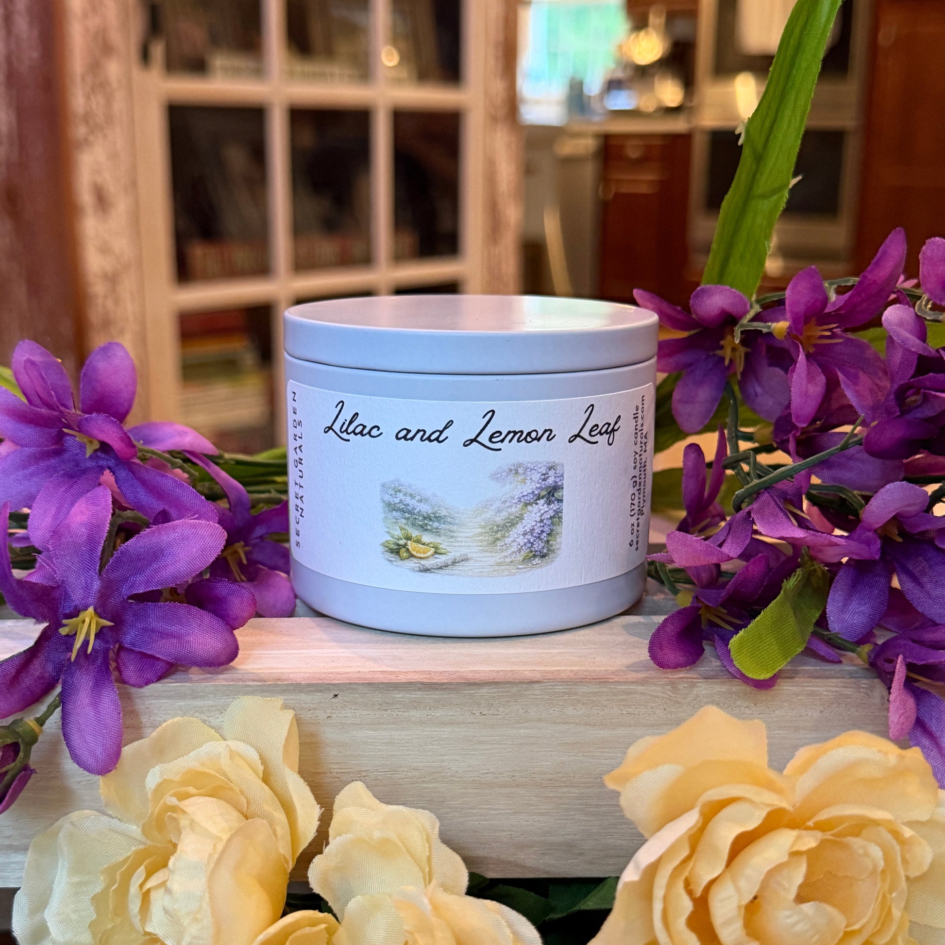 Lilac and Lemon Leaf candle tin  with a label surrounded by purple and yellow flowers in a kitchen setting