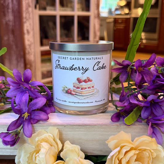 Candle labeled 'Strawberry Cake' with purple and yellow flowers in the foreground