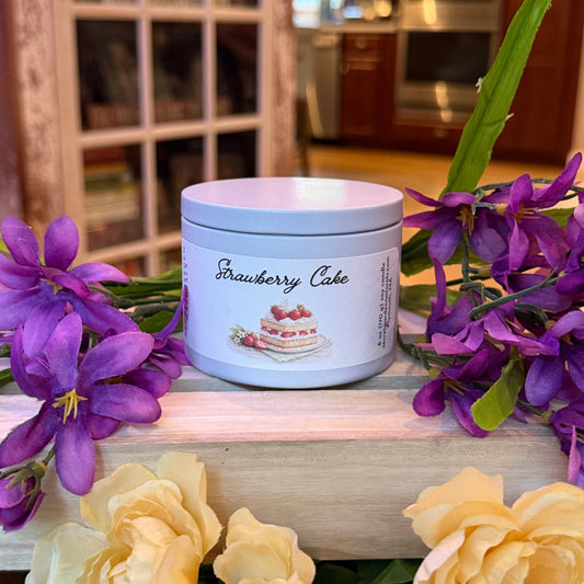 Candle tin  labeled 'Strawberry Cake' with purple and yellow flowers in a blurred indoor setting