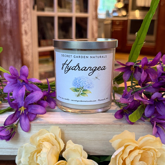 Hydrangea candle on a wooden surface with purple and yellow flowers.