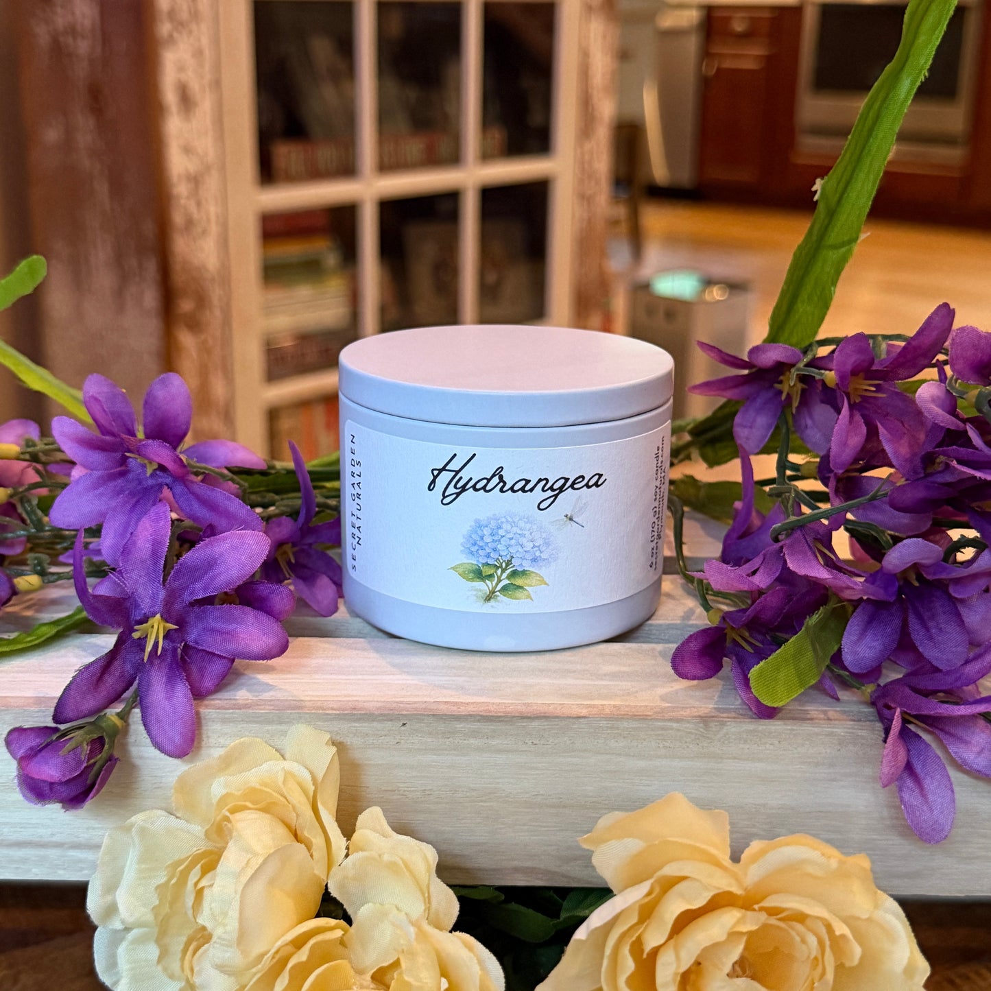Hydrangea candle in a tin with purple and yellow flowers in a decorative setting