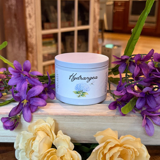 Hydrangea candle in a tin with purple and yellow flowers in a decorative setting