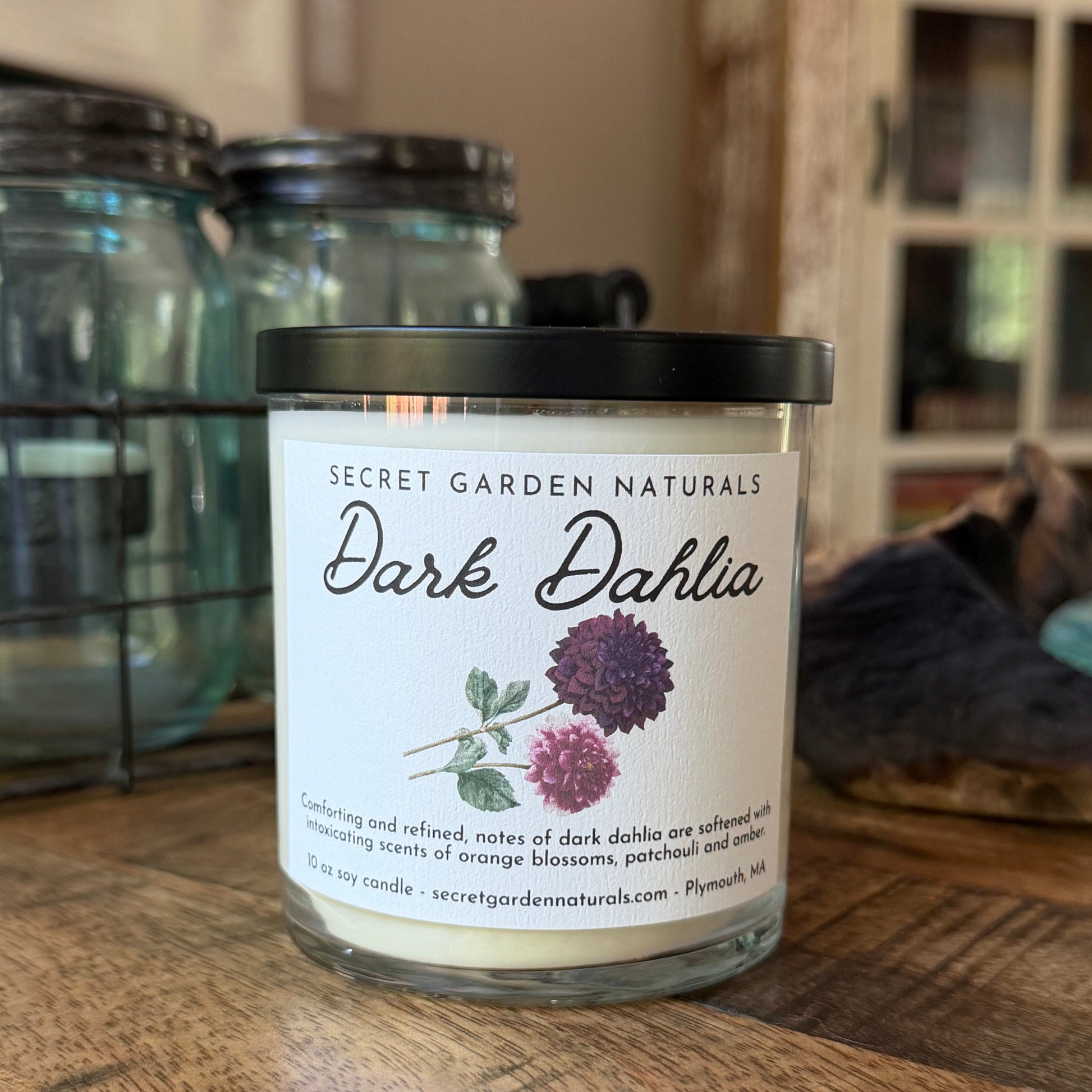 Candle labeled 'Dark Dahlia' from Secret Garden Naturals on a wooden surface.
