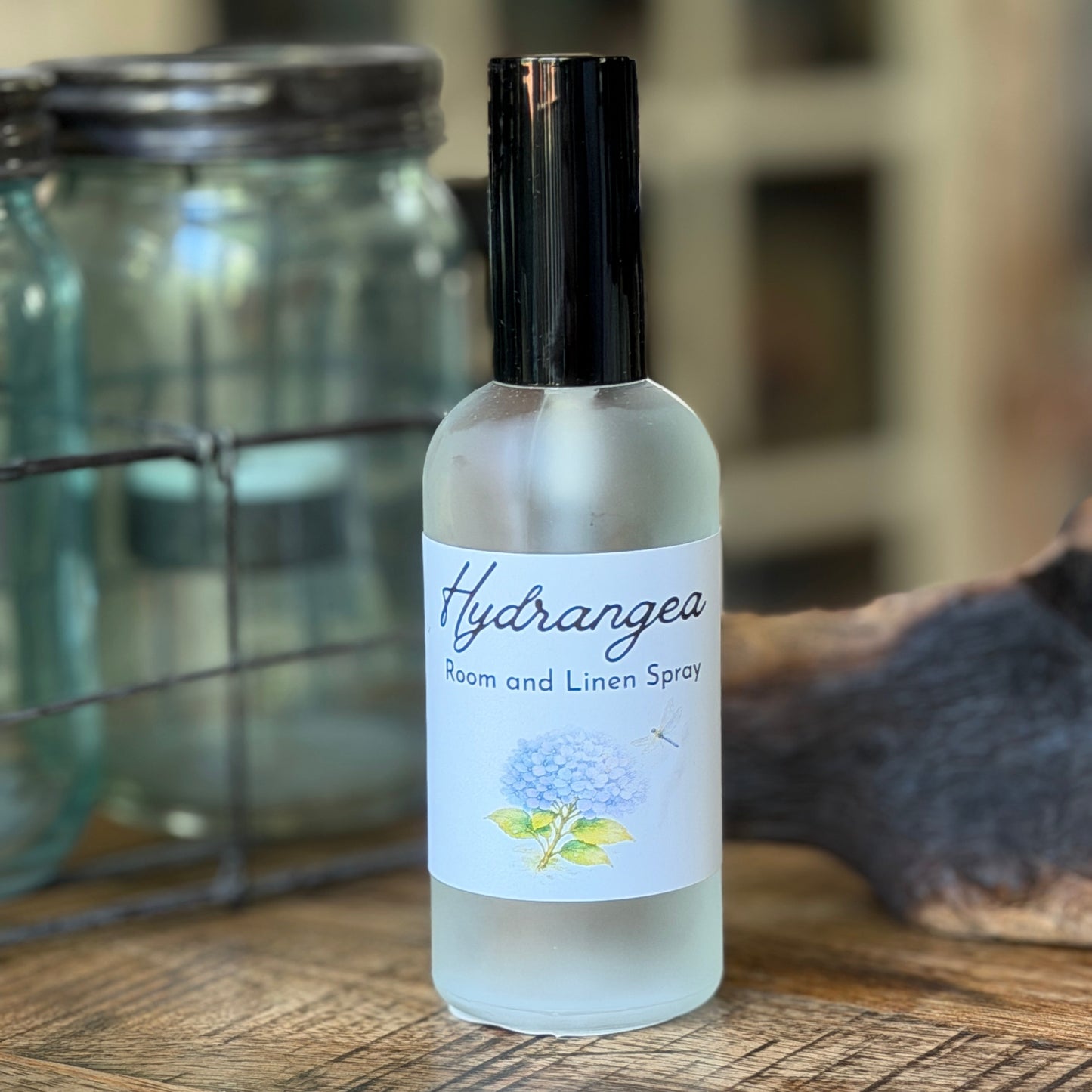 Bottle of Hydrangea room / linen spray on a wooden surface with a blurred background