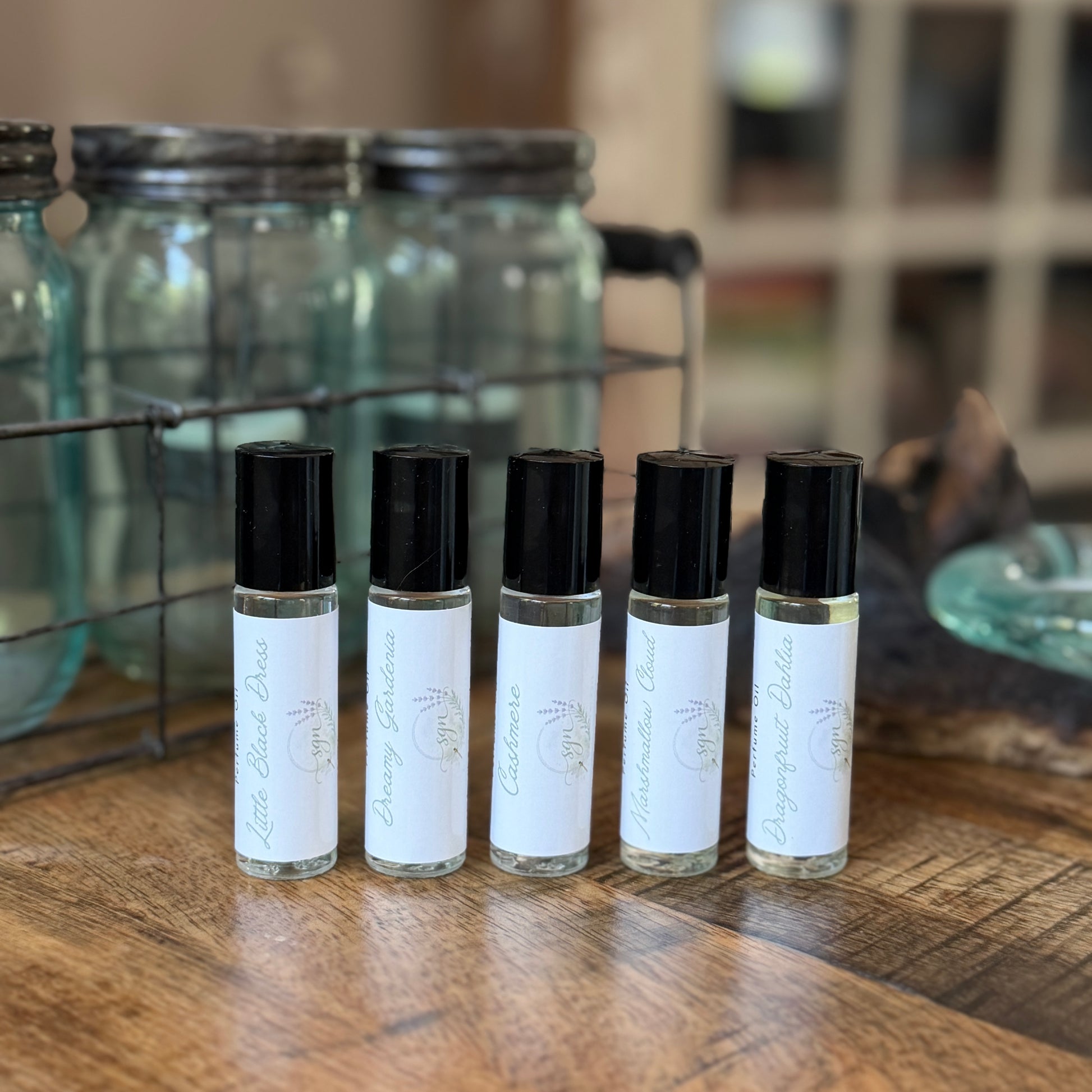 Five small rollerball bottles with black caps on a wooden surface.