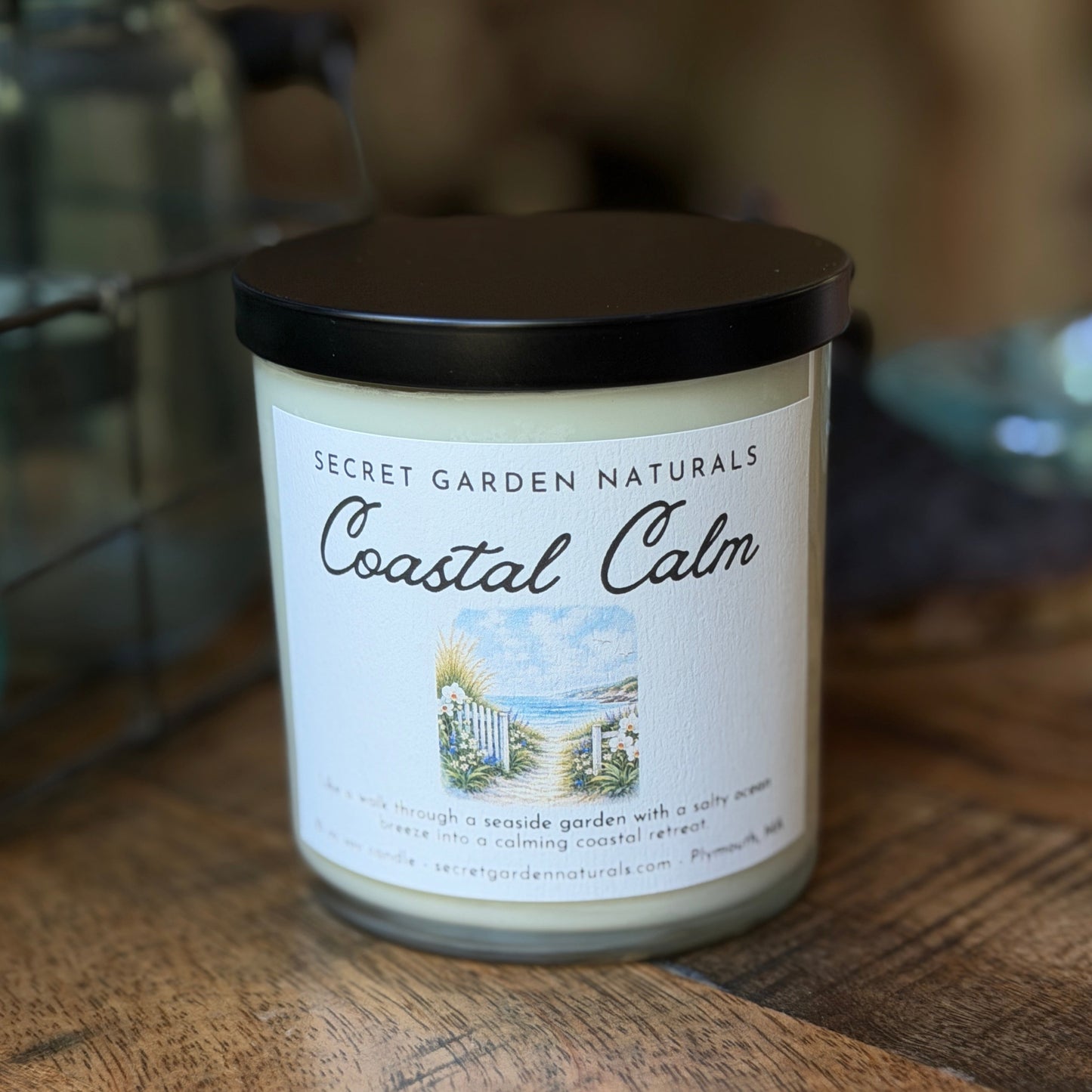 Candle labeled 'Coastal Calm' from Secret Garden Naturals on a wooden surface.