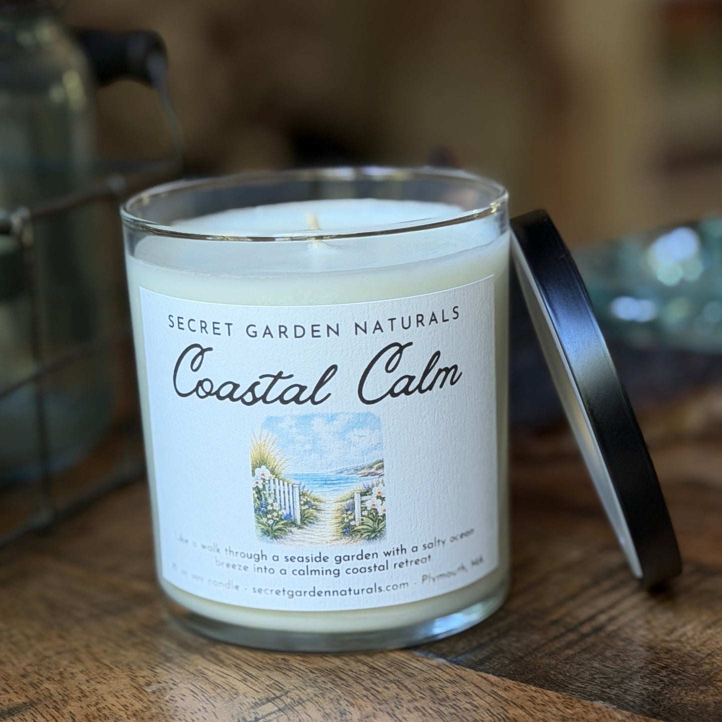 Candle labeled 'Coastal Calm' from Secret Garden Naturals on a wooden surface.