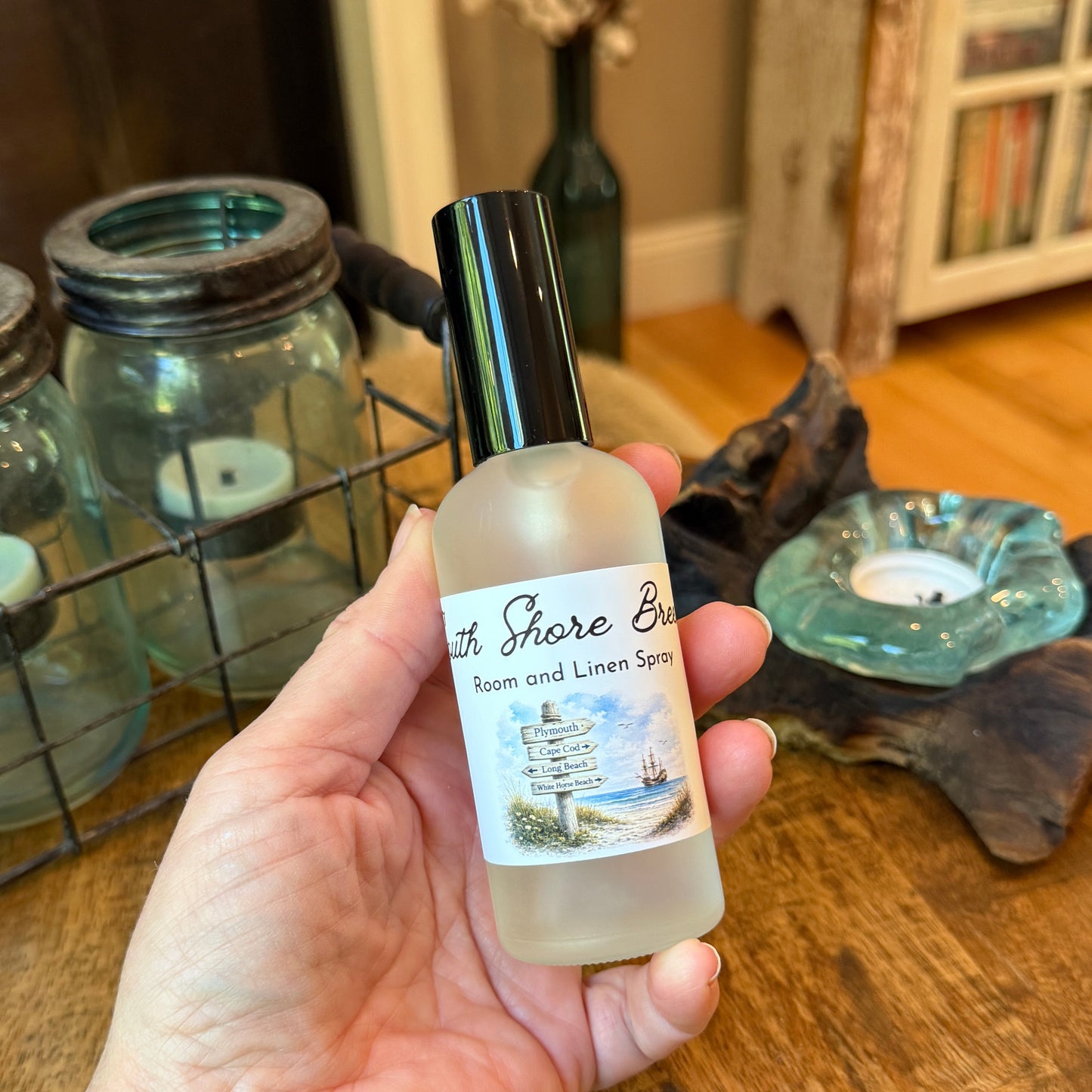Hand holding a bottle of 'South Shore Breeze' room and linen spray on a wooden surface.