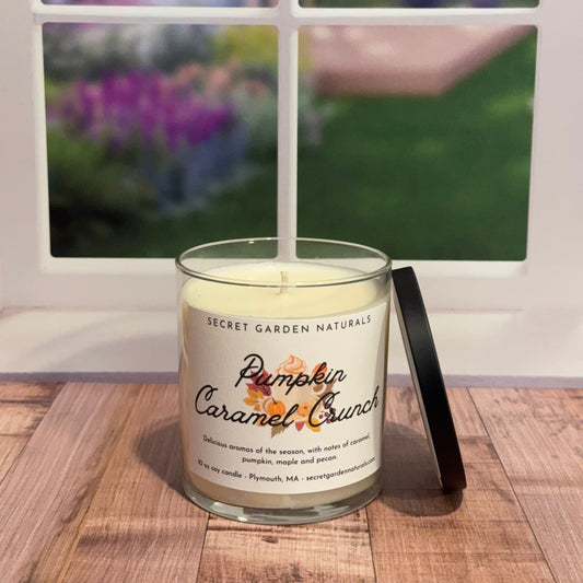 Candle labeled 'Pumpkin Caramel Crunch' on a wooden surface with a blurred outdoor background