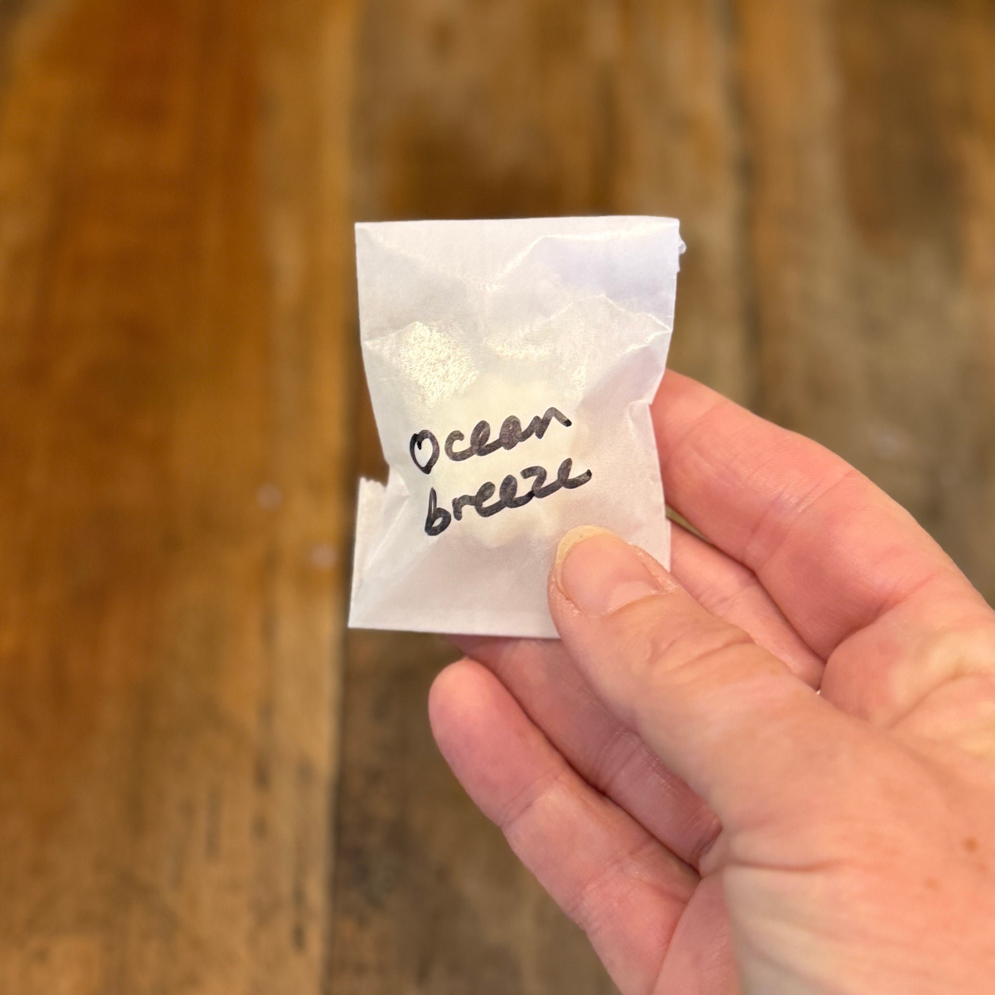 Hand holding a small white packet labeled 'Ocean Breeze' against a wooden background