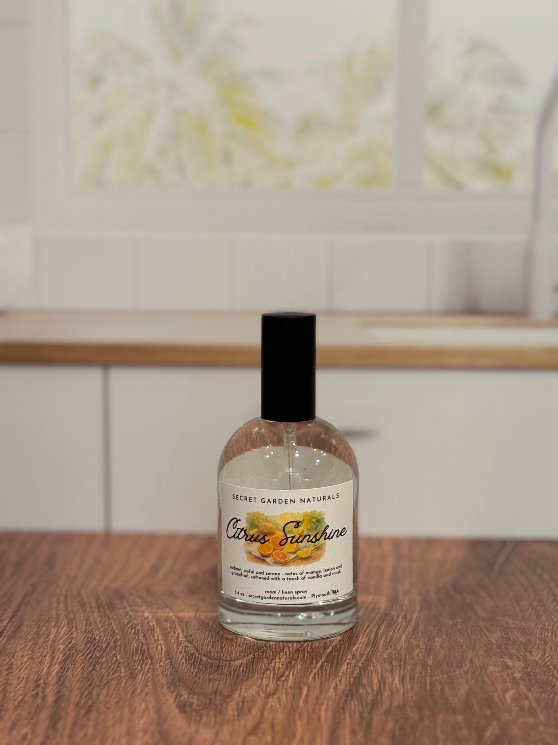 Bottle of 'Citrus Sunshine' room/linen spray on a wooden surface with a blurred kitchen background