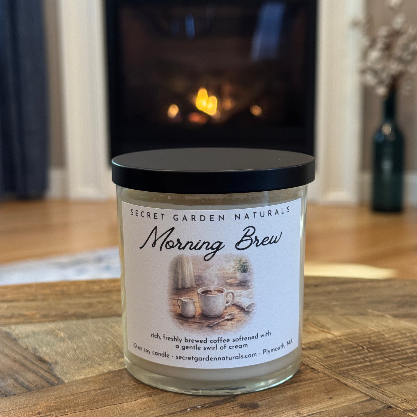 Candle labeled 'Morning Brew' on a wooden surface with a fireplace in the background