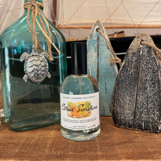 Bottle of 'Citrus Sunshine' room spray with decorative bottles and turtle ornament on a wooden surface.