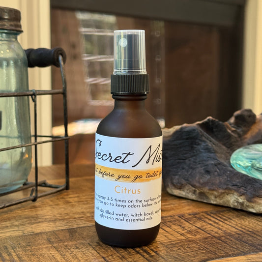 Bottle of 'Secret Mist' toilet spray on a wooden surface with a blurred background