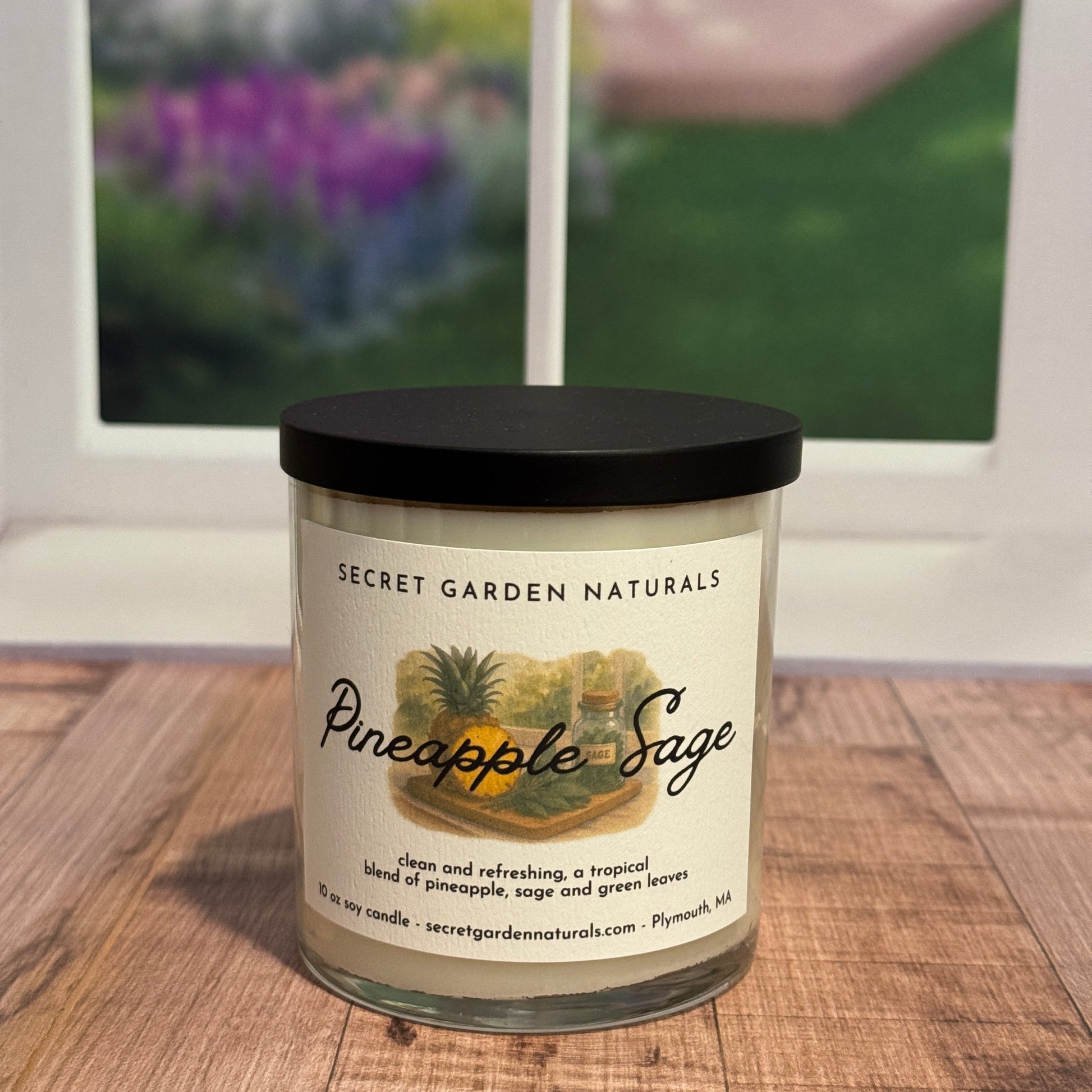 Candle labeled 'Pineapple Sage' on a wooden surface with a blurred window in the background