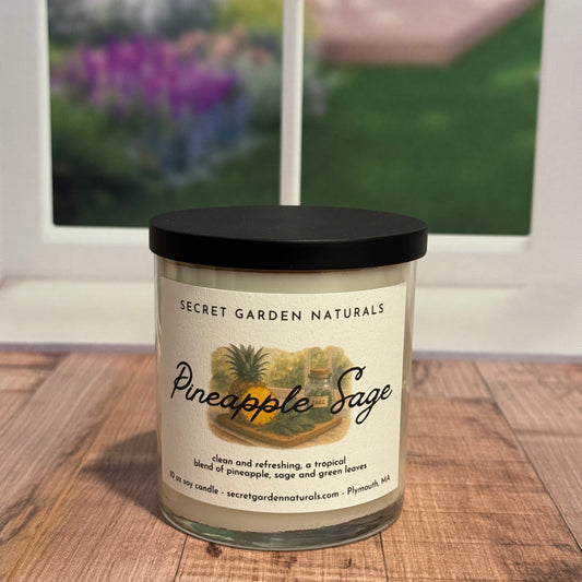 Candle labeled 'Pineapple Sage' on a wooden surface with a blurred window in the background