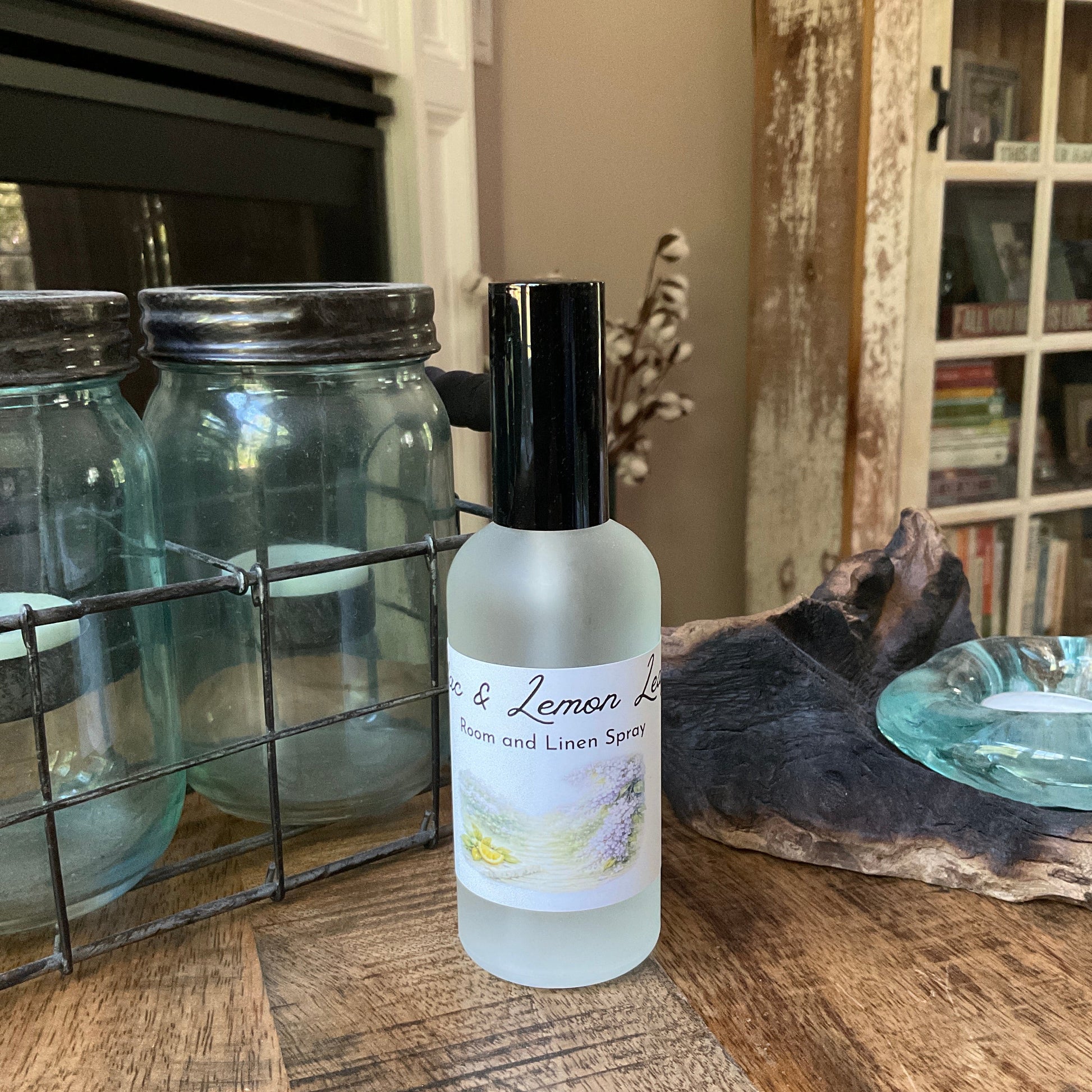 Bottle of lilac and lemon leaf room and linen spray on a wooden table with jars and books in the background