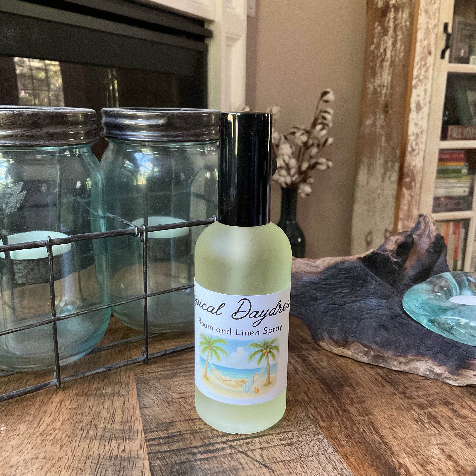 Glass bottle of tropical daydream room and linen spray on a wooden table with jars and books in the background